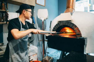 um pizzaiolo colocando uma pizza num forno de lenha