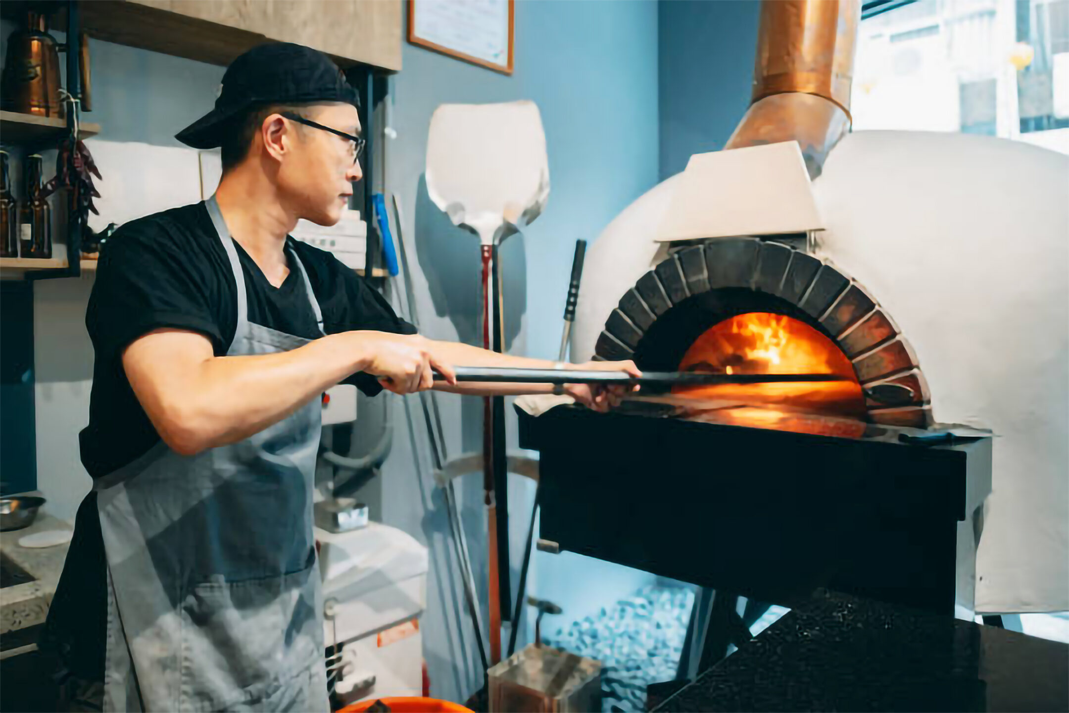 um pizzaiolo colocando uma pizza num forno de lenha